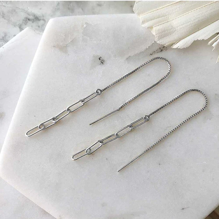 Silver chain threader earrings displayed on marble. The earrings are compose of five narrow links, the first of which is attached to a long piece of fine box chain with an earring post at one end. 