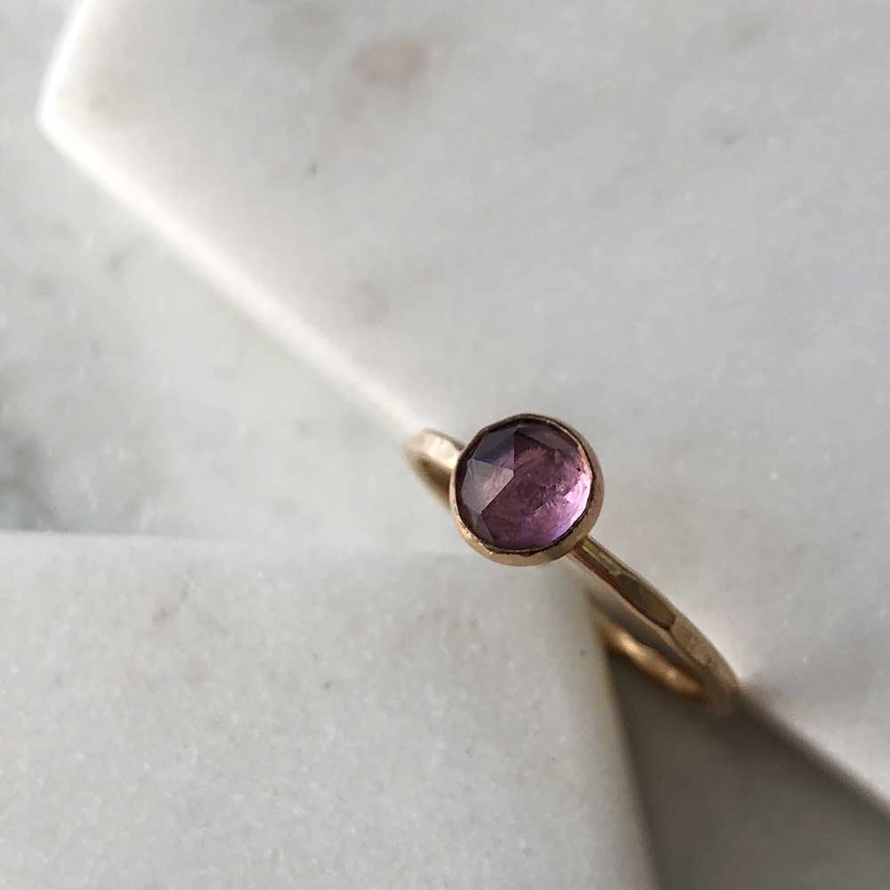 A gold-filled ring with a hammered band and a bezel-set amethyst displayed on marble. 