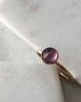 A gold-filled ring with a hammered band and a bezel-set amethyst displayed on marble. 