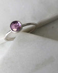 One silver with a hammered band and a bezel-set amethyst displayed on marble. 