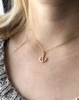 A gold-filled, loosely anchor-shaped pendant on a fine chain, worn by a model. It hangs in the divot between her collarbones.  
