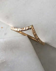 A finely textured gold-filled ring with a pointed chevron. Displayed on marble. 