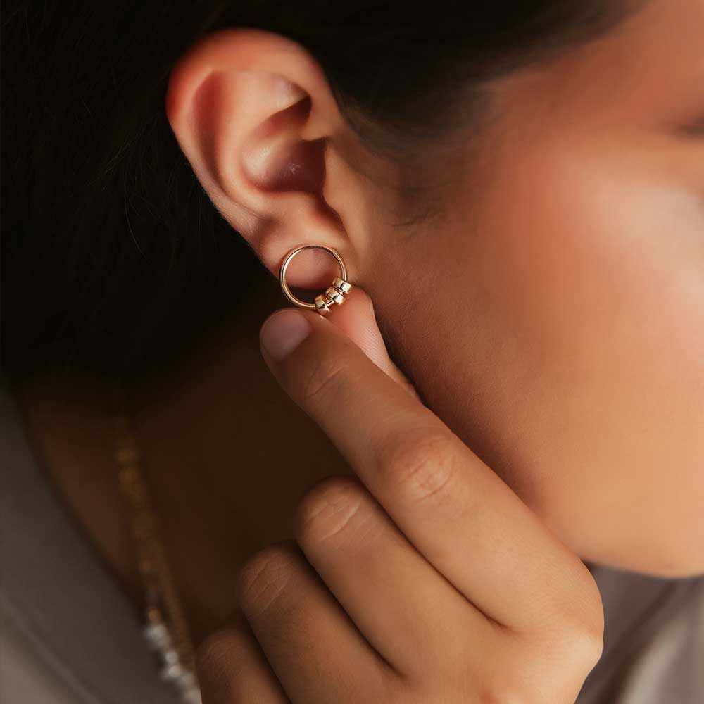 A gold-filled circle stud earring with three polished gold-filled beads, worn by a model. 