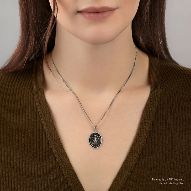 A Sterling Silver Pyrrha talisman With a Talisman depicting a tall mountain with a sun rising over it, including the text "Amor fati" written beneath it | on model