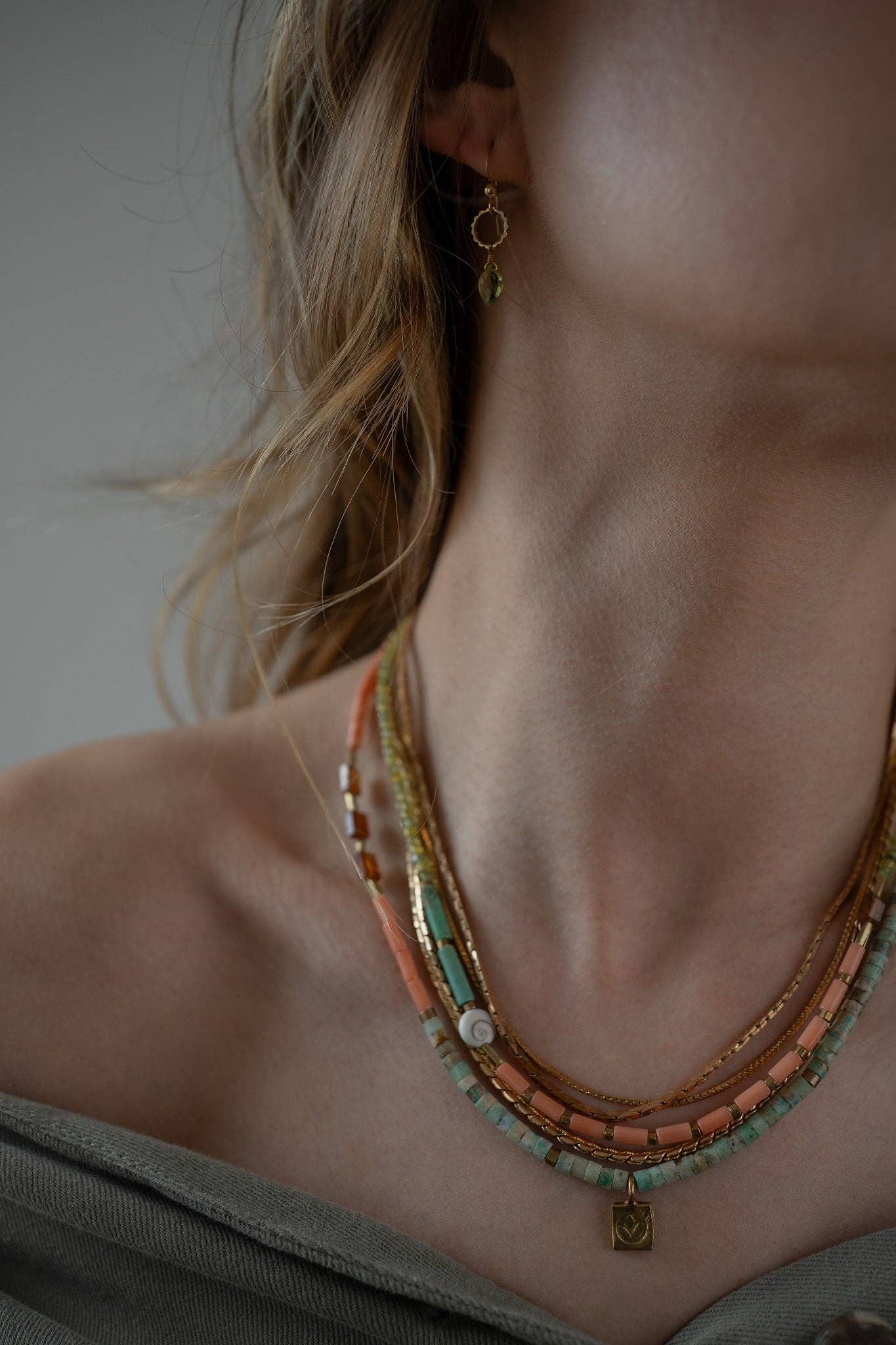 Belinay Necklace featuring a combination of shiva shell, dyed coral, hand-cut gemstones, and brass accents. With multiple strands and a variety of colours including Hessonite, Peridot, Yellow Jade, Turquoise, Dyed Coral, and Shiva Shell. | on model