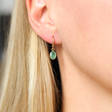 These 14k Yellow Gold hoops feature a delicate oval emerald charm.  | on model