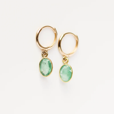 These 14k Yellow Gold hoops feature a delicate oval emerald charm. 