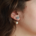 Silver pewter petal-shaped stud earrings with a freshwater pearl suspended behind the lobe | on model