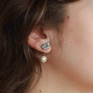 Silver pewter petal-shaped stud earrings with a freshwater pearl suspended behind the lobe | on model