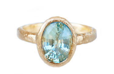 An oval blue-green sapphire, alive with the shifting colours of water, is cradled in hand-sculpted 14k yellow gold.