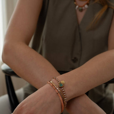 This unique bracelet features a combination of Hessonite, Moonstone, brass-edged Turquoise, and a 14K gold-plated brass coin pendant, all showcased in a striped pattern. | on model