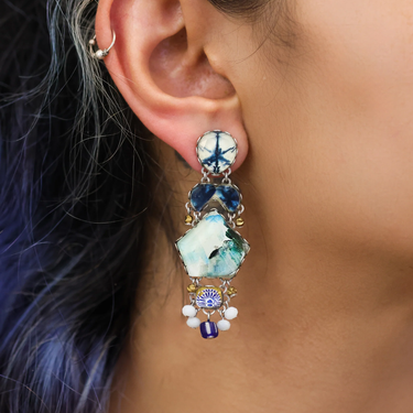 Plated Sterling Silver Earring Featuring an Intricate Design with mixes of multicoloured Textile thread and multiple sizes of gemstones and beads. The main colours include tones of blue and and White. The centerpiece of this earring is a large gemsone in the shape of a pentagon | on model