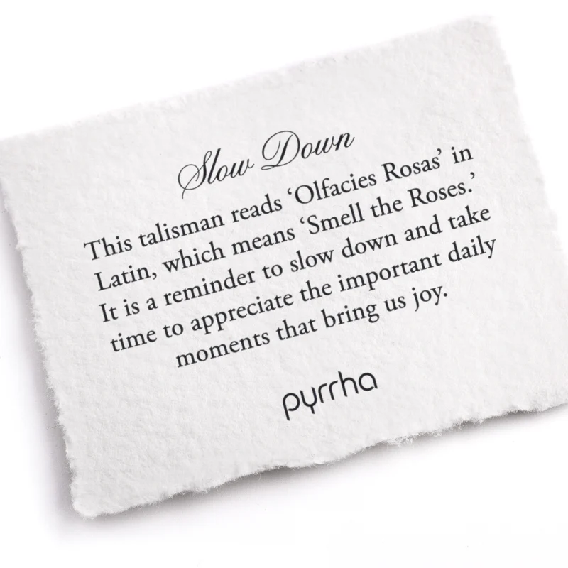 A Pyrrha note describing the Slow Down talisman. It reads, "This talisman reads 'Olfacies Rosas' in Latin, which means 'Smell the Roses.' It is a reminder to slow down and take time to appreciate the important daily moments that bring us joy."