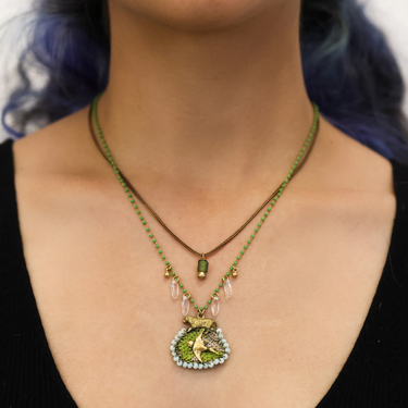Plated Sterling Silver Necklace predominantly featuring a texttile design primarily black and yellow, with a tiger above it. Connected to it is  2  thin chains with small white gems hanging and a small green gemstone in the middle of the chains  | on model