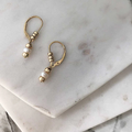 14k yellow Gold drop earrings with a leverback mechanism that allows for gold beads to be moveable. connected to the earring is two more beads encompassing a white pearl