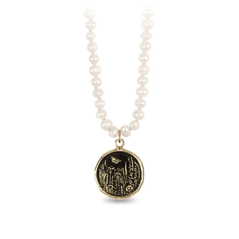Knotted ivory freshwater pearl necklace with a 14k Yellow gold talisman depicting a Butterfly flying over a field of varying flora and plants