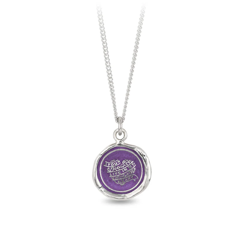 Sterling Silver necklace with a violet background under a talisman depicting a heart wrapped in ribbons that read out, "you live in my heart"