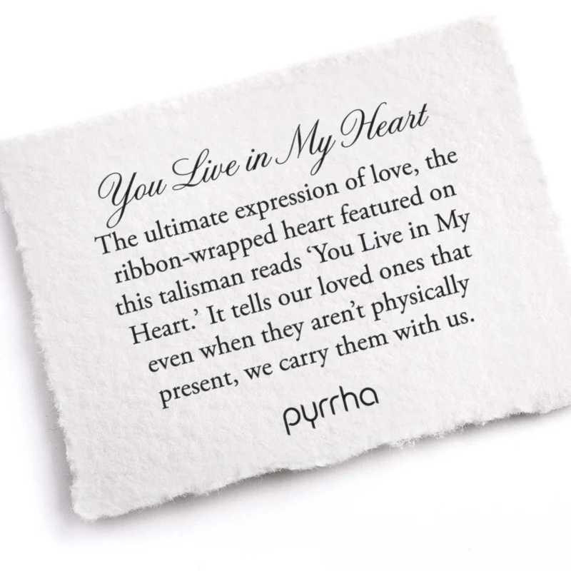 A Pyrrha Note describing the You Live in My Heart talisman. it reads, "The ultimate expression of love, the ribbon-wrapped heart featured on this talisman reads 'You Live in My Heart.' It tells our loved ones that even when they aren't physically present, we carry them with us."