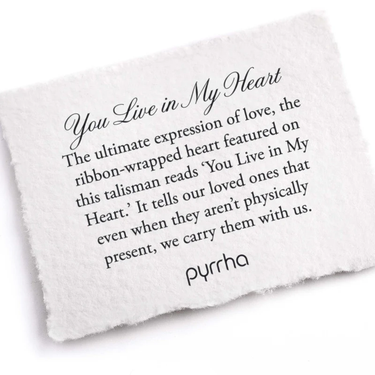 A Pyrrha Note describing the You Live in My Heart talisman. it reads, "The ultimate expression of love, the ribbon-wrapped heart featured on this talisman reads 'You Live in My Heart.' It tells our loved ones that even when they aren't physically present, we carry them with us."