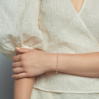 Ten small oval pearls spaced in an alternating pattern on a delicate 14-karat gold chain bracelet.  | on model