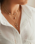 A necklace with three white pearls (flanked by polished gold-filled beads) staggered about an inch apart on fine gold-filled chain. Worn by a model as the shortest of a collection of necklaces.