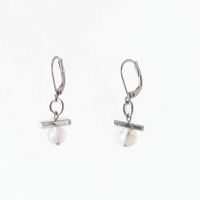 Pictured: drop earrings on white background, composed of a surgical steel leverback closure connected by a jump loop to a horizontal pewter bar set atop a pale agate stone. The agates are spherical and polished, and appeared to be drilled through, as the silver-coloured disc at the end of the bead pin is slightly visible at the bottom.