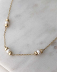 A necklace with three white pearls (flanked by polished gold-filled beads) staggered about an inch apart on fine gold-filled chain. Displayed on marble. 