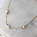 A necklace with three white pearls (flanked by polished gold-filled beads) staggered about an inch apart on fine gold-filled chain. Displayed on marble.  | Magpie Jewellery