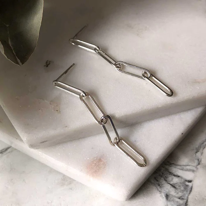 Silver chain earrings displayed on marble. The earrings are composed of four narrow oval links, the first of which is attached to a stud post. 