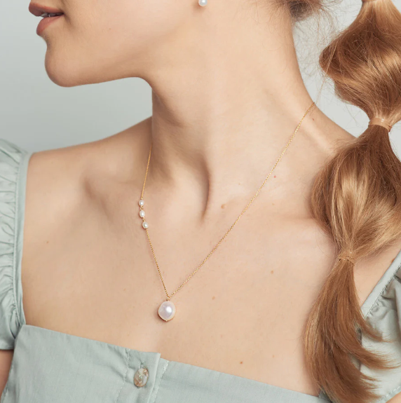A large baroque pearl pendant anchors a 14-karat gold chain with a trio of baby keshi pearl on one side. | on model