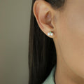 Pearl studs with a vibrant Emerald nested along the side of two lustrous pearls creating cluster pearl earrings | on model