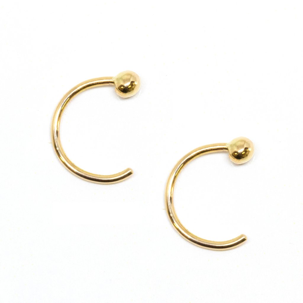 A pair of 14k gold huggies in a pull-through style with a solid gold ball in front.