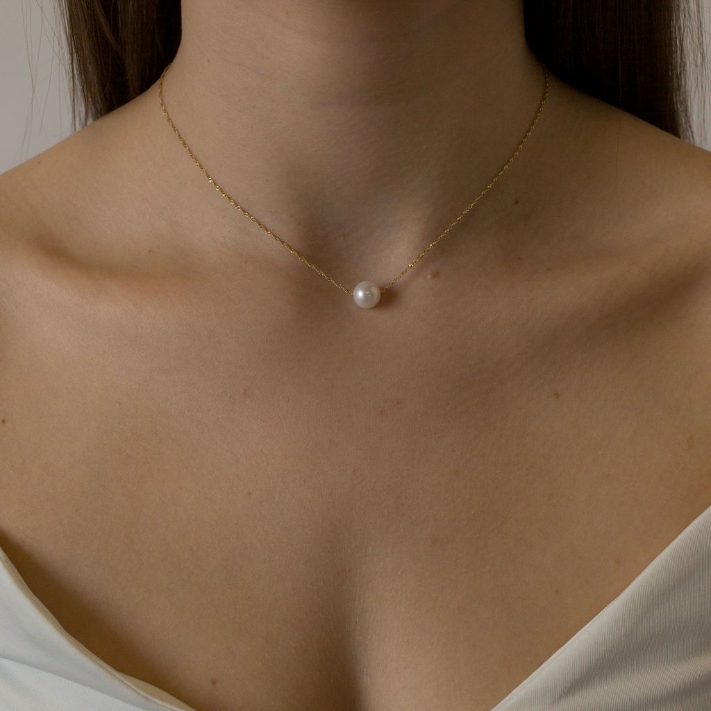 A single luscious round white pearl on a delicate 14-karat shimmering gold chain | on model