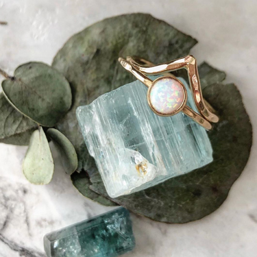 Two rings: a hammered gold-filled ring with a pointed chevron, and a hammered gold-filled ring with a bezel-set opal. Displayed with leaves and crystals.  | Magpie Jewellery