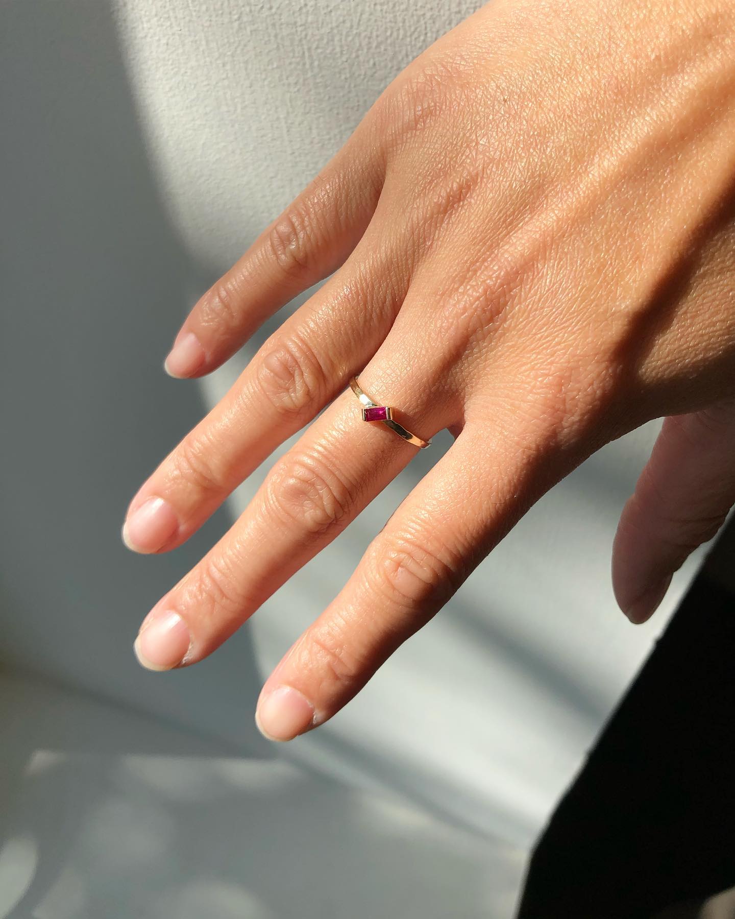 A single baguette shaped ruby set on an angle on a slim hammered gold band. | on model