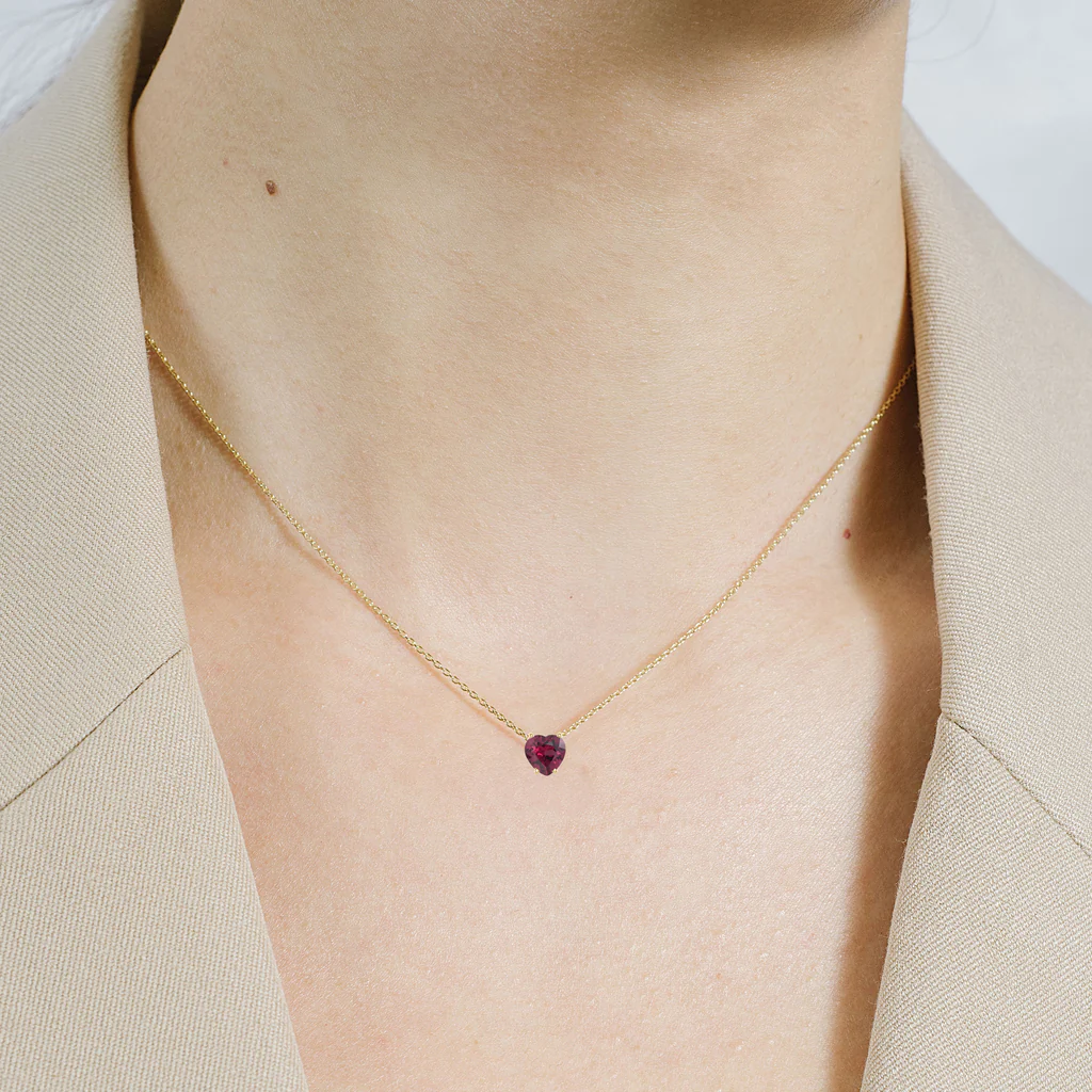 A vibrant heart shaped gemstone pendant on a dainty 14-karat gold chain.  | on model