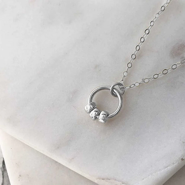 A silver circle pendant with three polished silver beads. Hung from a fine silver chain and displayed on marble.  | Magpie Jewellery