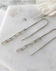 Silver chain threader earrings displayed on marble. The earrings are compose of five narrow links, the first of which is attached to a long piece of fine box chain with an earring post at one end. 