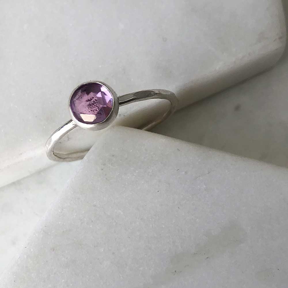 One silver with a hammered band and a bezel-set amethyst displayed on marble. 