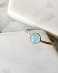 A hammered gold-filled band set with a pale blue aquamarine in a bezel. Displayed on marble. 