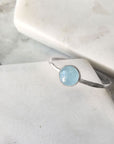 A hammered silver band set with a pale blue aquamarine in a bezel. Displayed on marble.