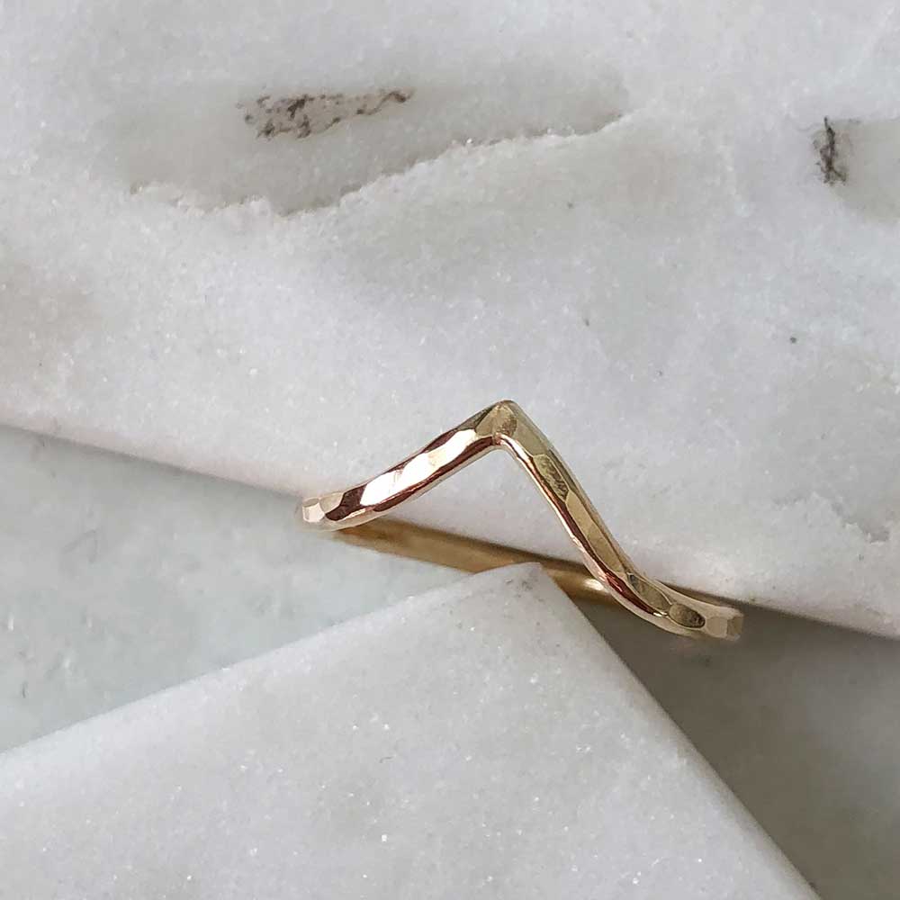 A hammered gold-filled ring with a pointed chevron. Displayed on marble. 