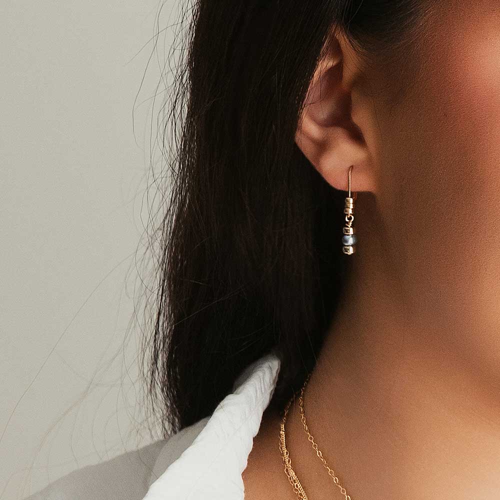 Dark pearl drop earrings on gold-filled leverback hooks embellished with three polished gold-filled beads each. Worn by model. Length hits corner of jaw. 
