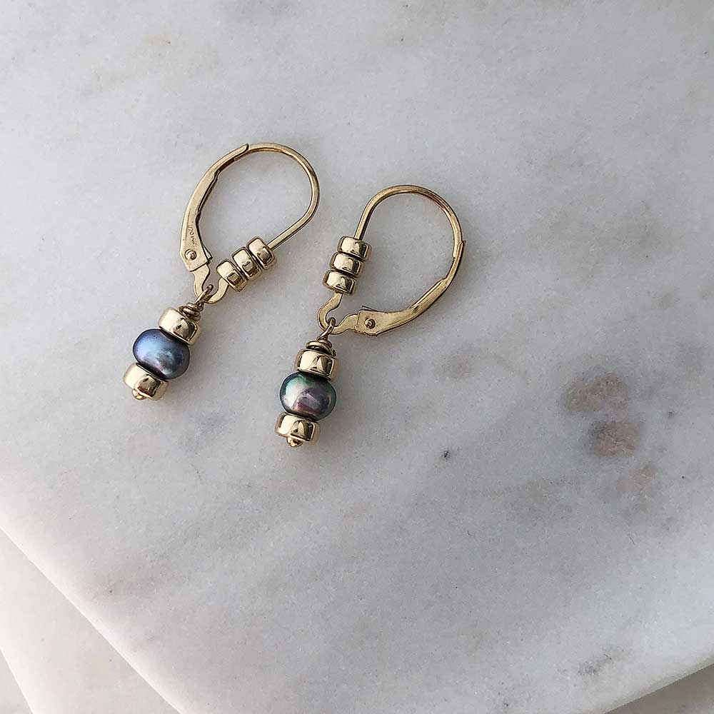 Dark pearl drop earrings on gold-filled leverback hooks embellished with three polished gold-filled beads each. Displayed on marble. 