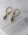 Dark pearl drop earrings on gold-filled leverback hooks embellished with three polished gold-filled beads each. Displayed on marble. 