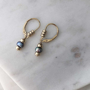 Dark pearl drop earrings on gold-filled leverback hooks embellished with three polished gold-filled beads each. Displayed on marble.  | Magpie Jewellery