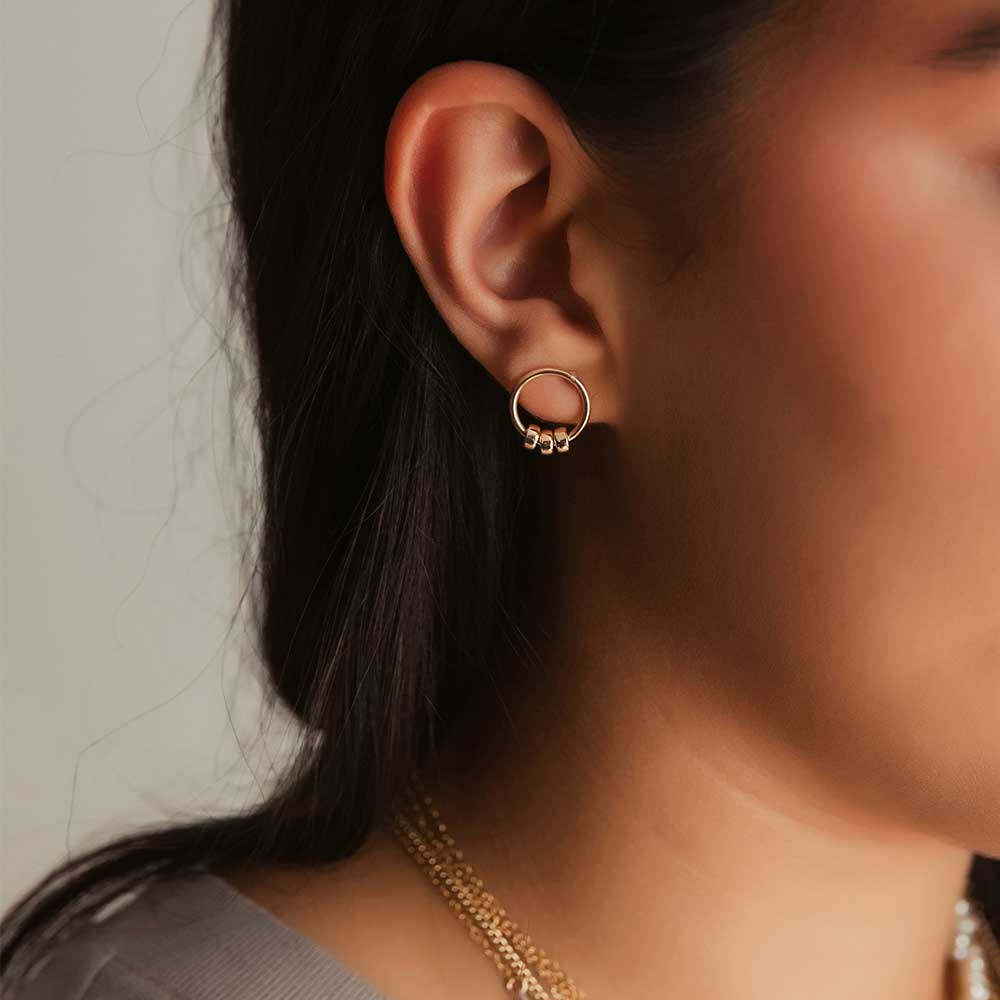 A gold-filled circle stud earring with three polished gold-filled beads, worn by a model. 